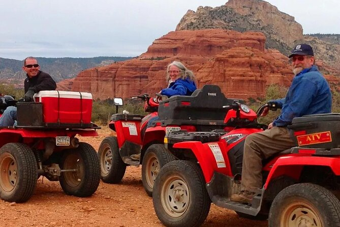 Three ATV riders smiling with the red rock formations behind them