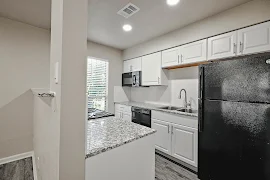 Modern kitchen with white cabinets, granite countertops, and black appliances in an apartment.