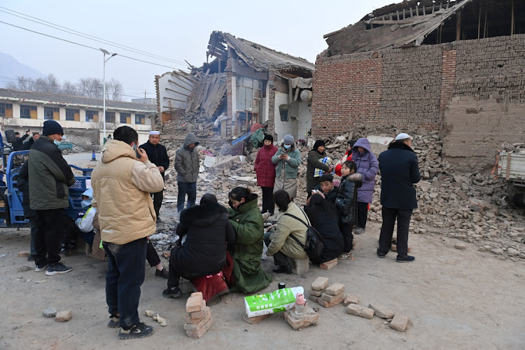 Residents keep warm by a fire next to damaged buildings at Dahejia town following the earthquake in Jishishan county, Gansu province, China, on December 19 2023. Picture: CNSPHOTO via REUTERS