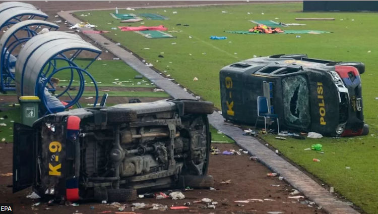 Damaged police vehicles lay on the pitch inside Kanjuruhan stadium