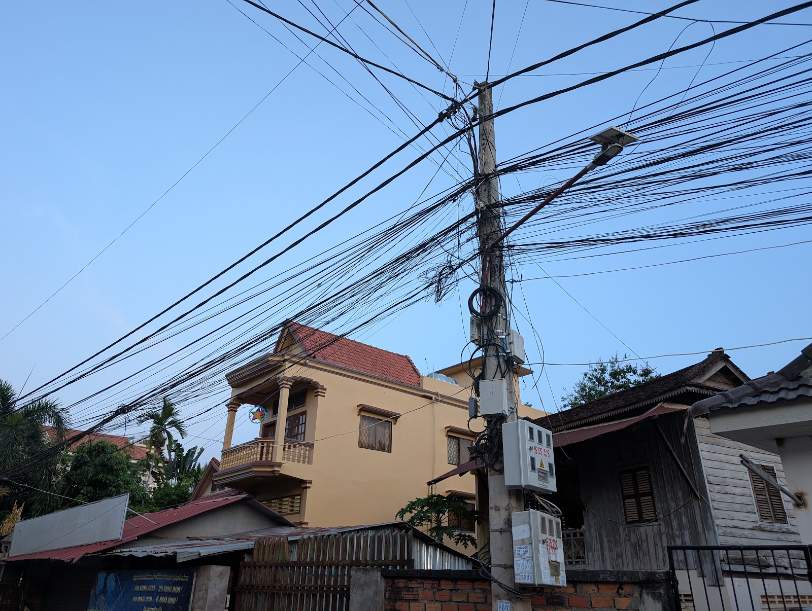 A utility pole on the sidewalk in front of some apartment
                 buildings that has a web of cables mostly going in three
                 directions: up and down the sidewalk and across the street.
                 The cables running above the sidewalk are arrayed in a
                 vertical pattern such that they almost look like a fence or a
                 wall suspended above the sidewalk.