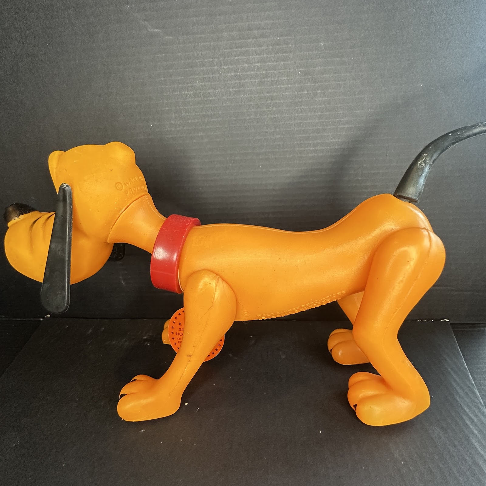 1960s Pluto blow-mold squeeze toy in yellow-orange vinyl with black rubber ears, nose, and tail, red collar, and original orange hang tag attached