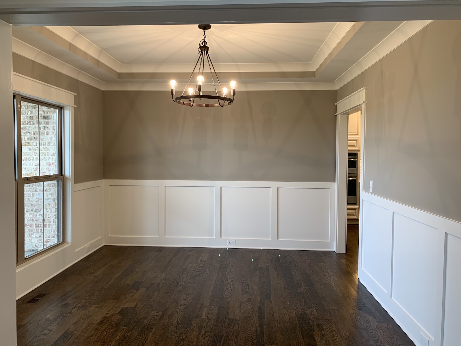 Interior room with dark wood flooring, tan walls, white wainscoting, a tray ceiling, and a black metal chandelier.