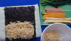Đặt bề nhám của miếng rong biển lên trên rồi lần lượt cho mì các loại rau, trứng, xúc xích và cuốn lại. Nhớ khi cuốn phải cuốn chặt tay để mì không bị rớt ra khi cắt khúc