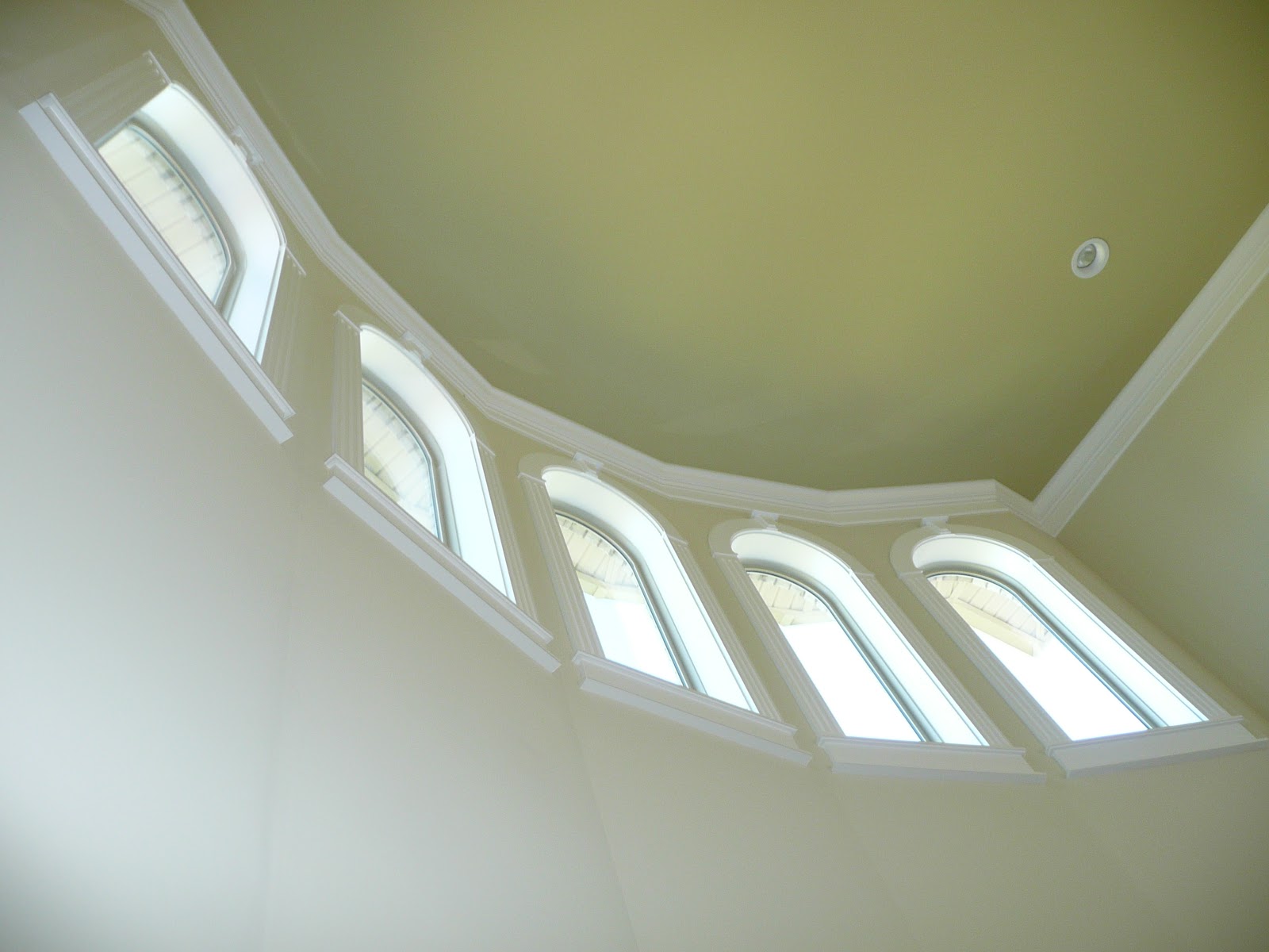 Low-angle view of five arched windows with white trim set into a curved tan wall.