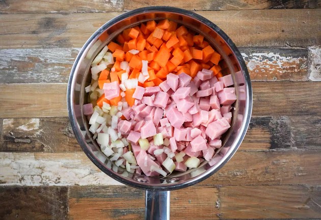 Adding onion, celery, carrots, and ham to the saucepan