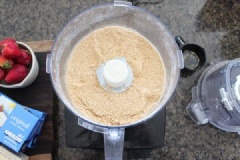 Trước tiên, bạn cho bánh quy vào máy xay nhuyễn. Thêm bơ đánh đều nào. Trải lớp hỗn hợp này vào khuôn nhé, dùng vật nặng ép mạnh xuống. Sau đó, cho kem phô mai, trộn với đường bột, vani, sữa cho nhuyễn mịn.