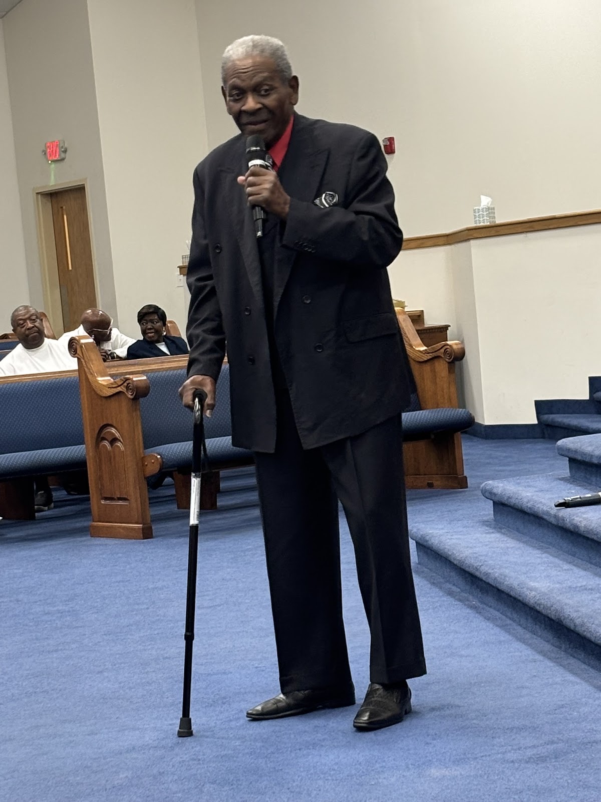 Honored elder with cane and microphone sharing a message at Homecoming Revival 2026