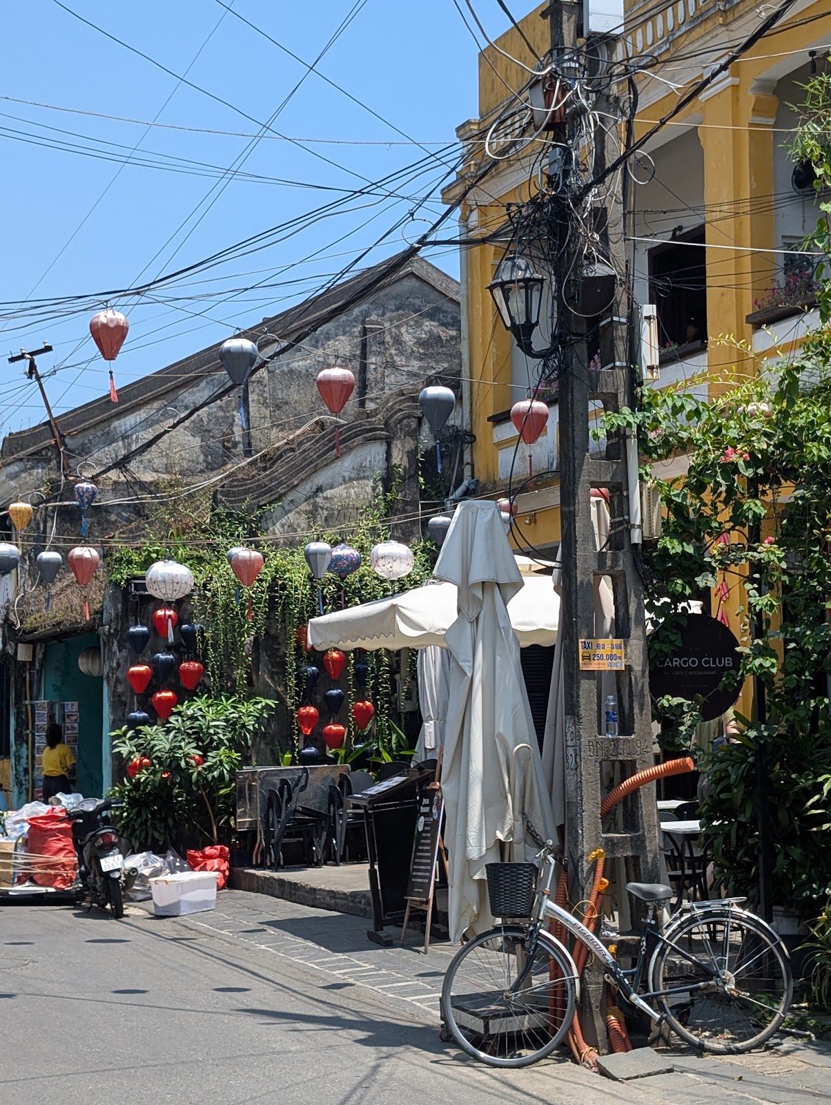 Photo of a concrete utility bowl with many criss-crossing wires.
                 A bicycle is leaning against the pole, and there are many paper
                 lanterns hanging around and a yellow building in the background.