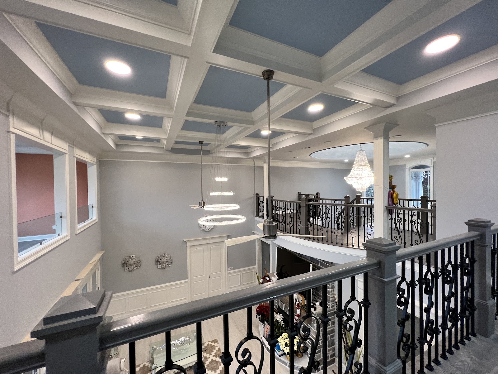 Spacious kitchen with light grey cabinetry, white marble-patterned tile flooring, a large island with a table extension, and multiple crystal chandeliers.