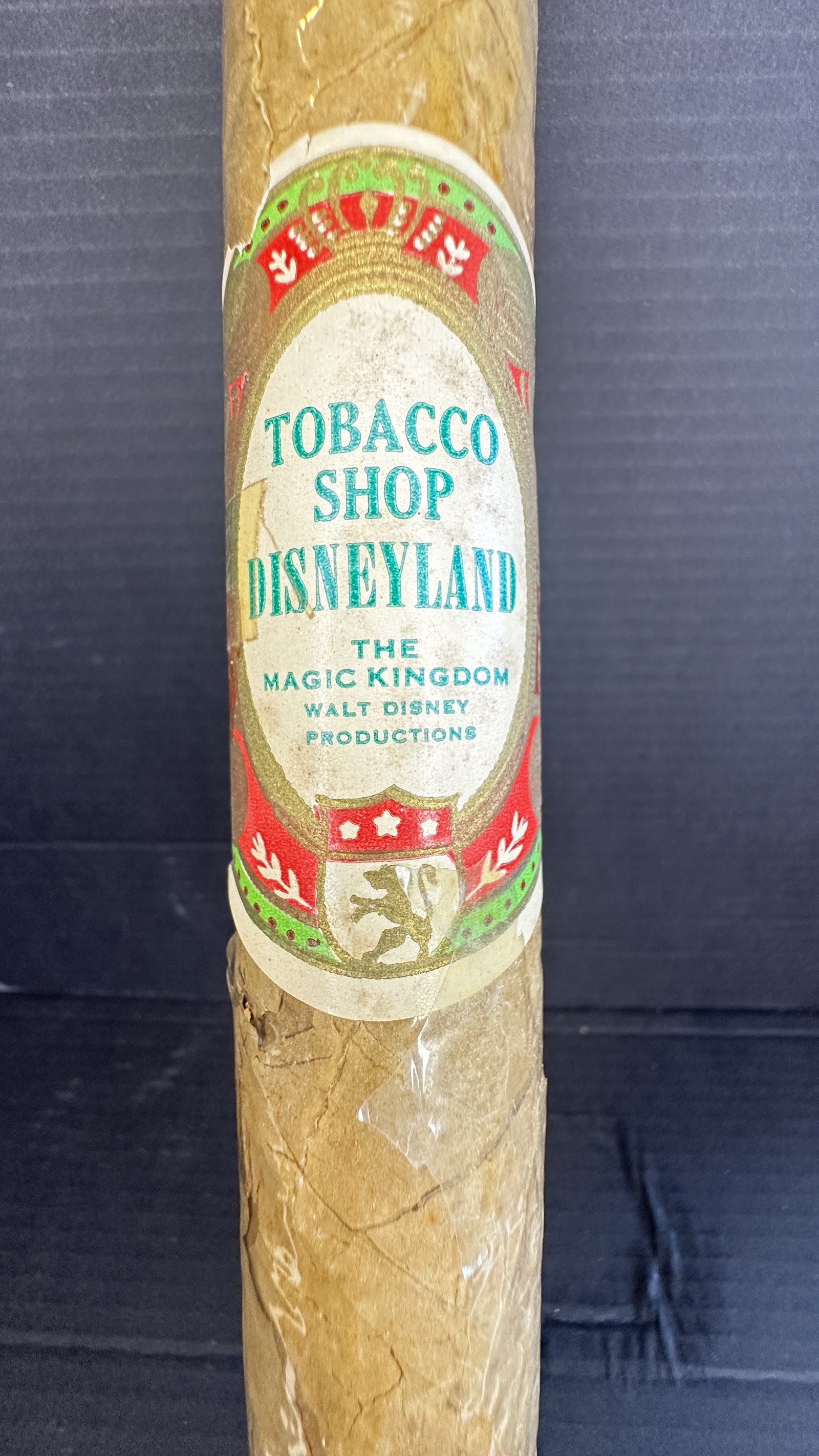 Vintage Disneyland Main Street Tobacco Shop souvenir cigar in cellophane sleeve with ornate heraldic gold lion crest label reading Tobacco Shop Disneyland Walt Disney Productions