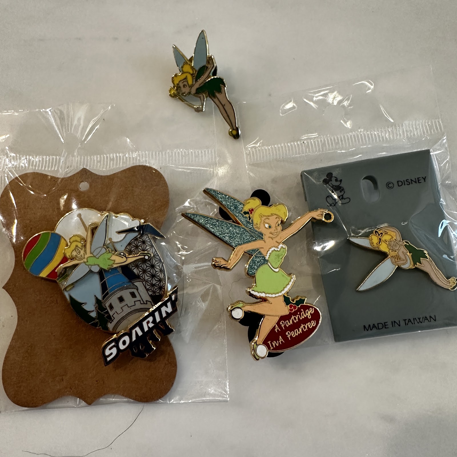Four Tinker Bell enamel pins including Soarin' attraction exclusive on leather-look card, 12 Days of Christmas Partridge in a Pear Tree pin, flying pose pin, and standing pose pin