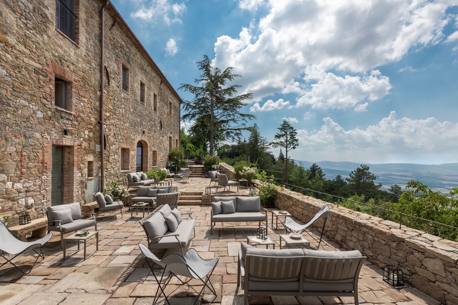 A stone terrace with loungers and chairs looking out over the Tuscan hills