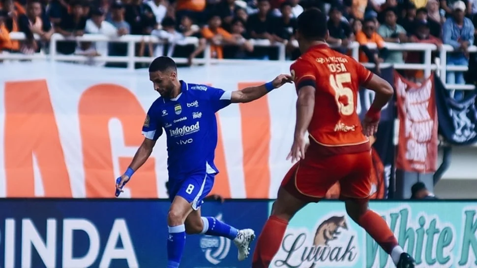 Pemain sepak bola profesional sedang berkompetisi di lapangan hijau dalam pertandingan liga.