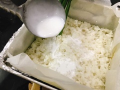 Sau 10 phút, lấy khay gạo ra khỏi lò, tạm thời nhấc lá dứa ra rồi chan đều 130ml nước cốt dừa lên trên bề mặt. Đặt lá dứa vào và cho khay gạo vào lò tiếp tục hấp ở nhiệt độ cao trong khoảng 20 phút. Sau 20 phút, lấy xôi ra khỏi lò, bỏ lá dứa đi. Dùng thìa ấn nhẹ, làm phẳng mặt xôi. Rồi tiếp tục cho vào lò hấp thêm khoảng 10 phút thì lấy ra và để nguội.