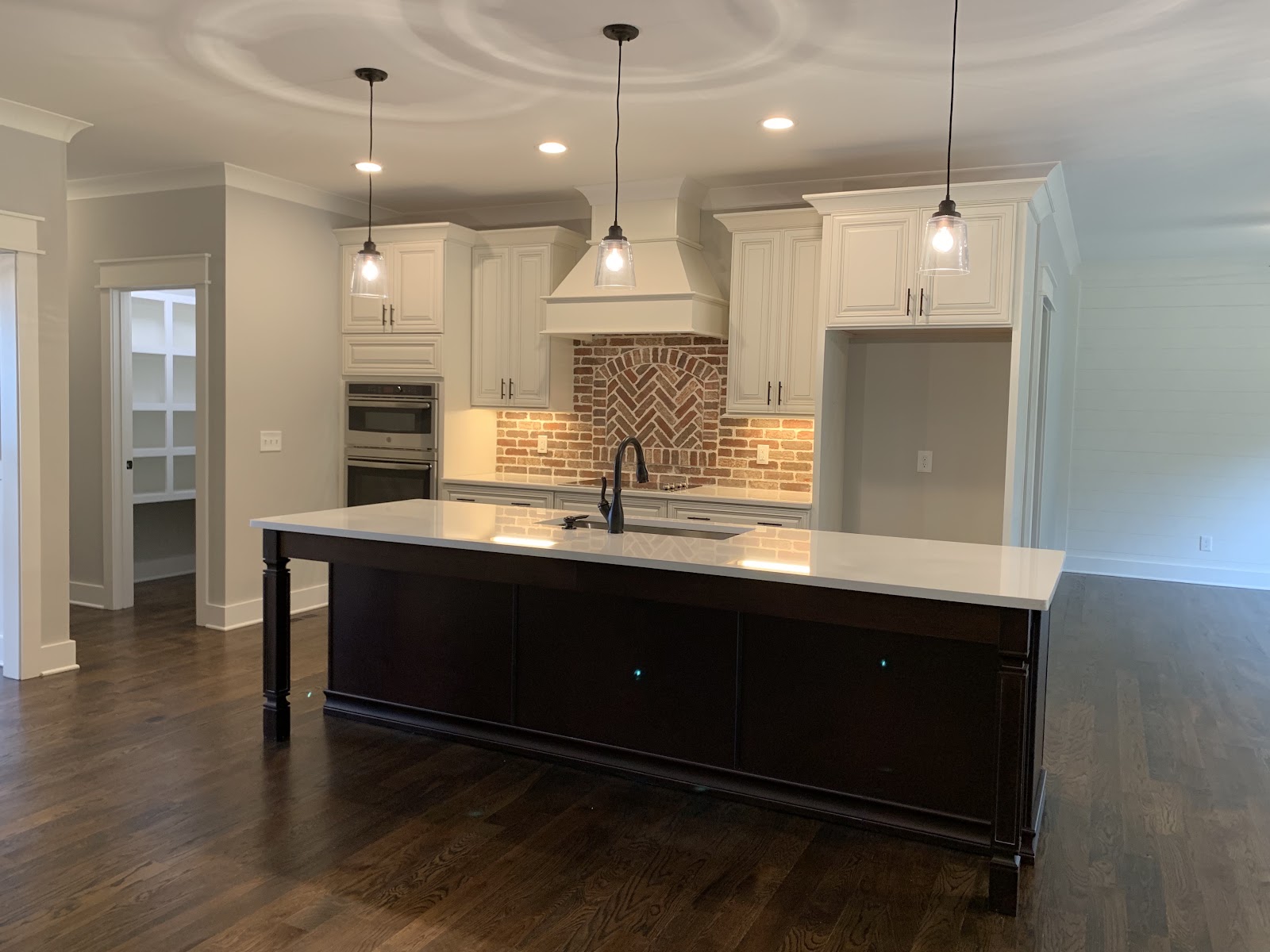 A kitchen featuring white cabinetry, a dark wood island with a white countertop, and a brick backsplash with a herringbone pattern.