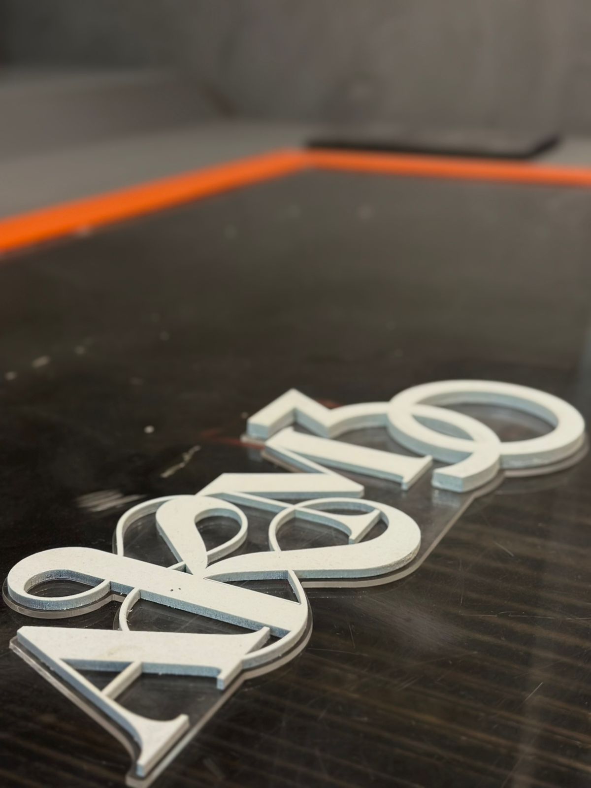 Letras 'AKM' em MDF branco sendo posicionadas sobre a base de acrílico transparente.