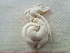 Qua thời gian ủ, bột nở lấy ra nhồi lại 3-5 phút cho bột mịn hơn. Chia bột thành 4 phần. Lăn bột thành từng thanh dài. Sau đó, gấp đôi lại. Uốn thanh bột thành hình chữa S để tạo hình thỏ. Dùng kéo cắt một ít ở phía trước làm miệng. Dùng tay ấn nhẹ phần bột bên trên cho dẹt xuống làm tai thỏ. Gắn hạt đậu đen hay đỏ làm mắt. Để thỏ lên giấy nến rồi xếp bánh vào xửng.