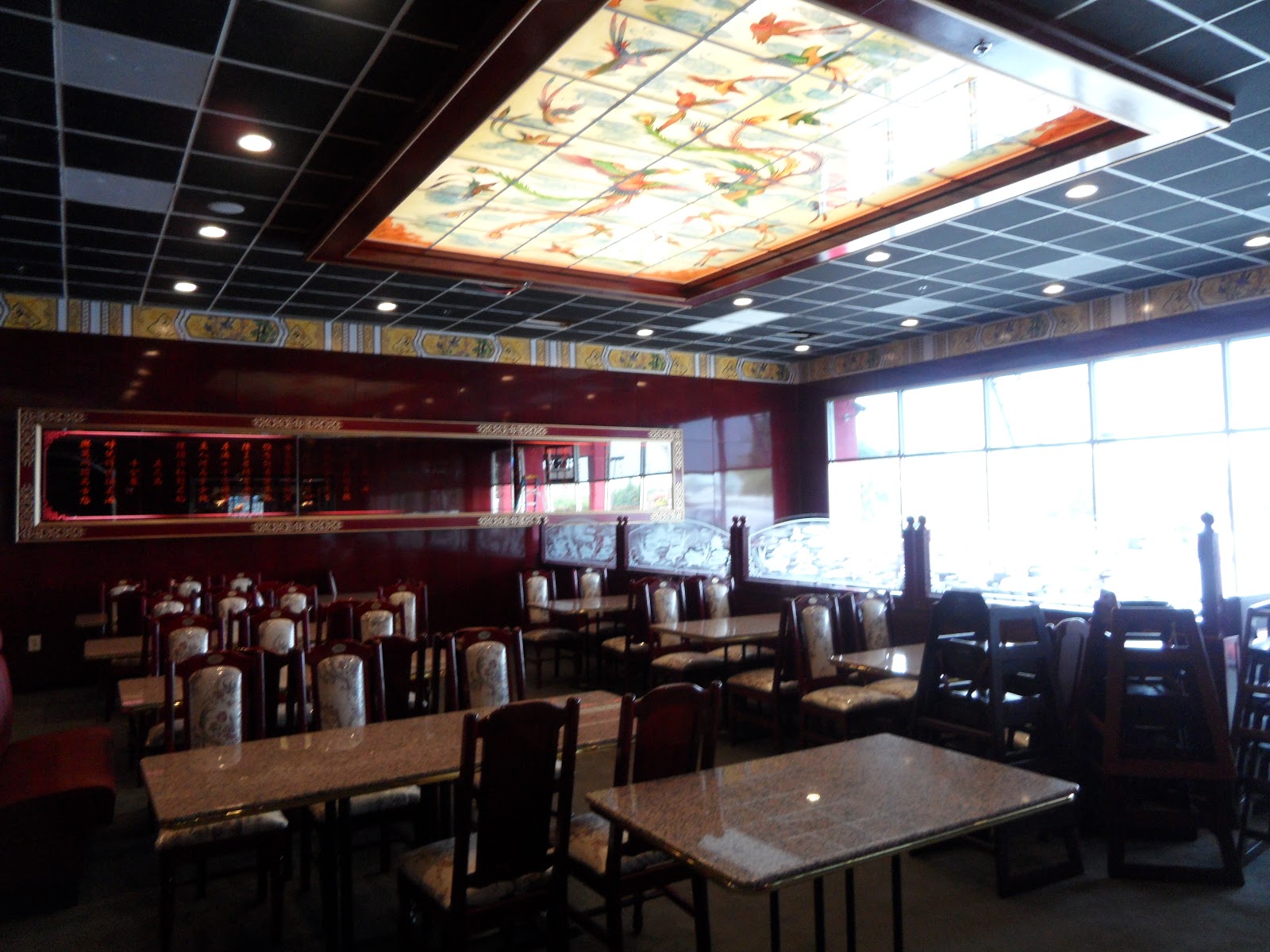 Restaurant dining room with granite-topped tables, chairs, and a large rectangular stained-glass ceiling light fixture.