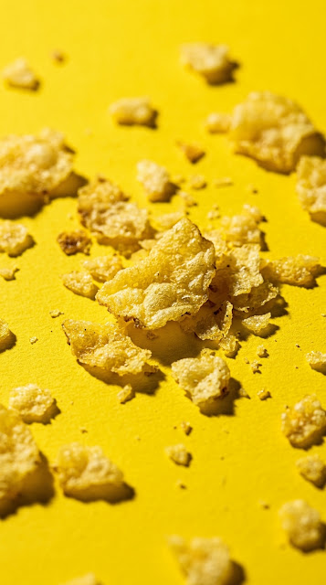 Macro view of broken potato chips and crumbs on a yellow surface - Free mobile Wallpaper