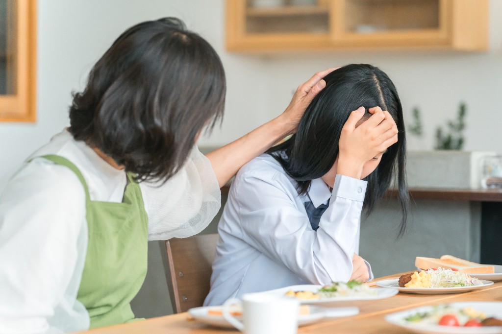 制服姿で顔を覆い俯く女子生徒と、そばで支える保護者のイメージ（写真はイメージです）