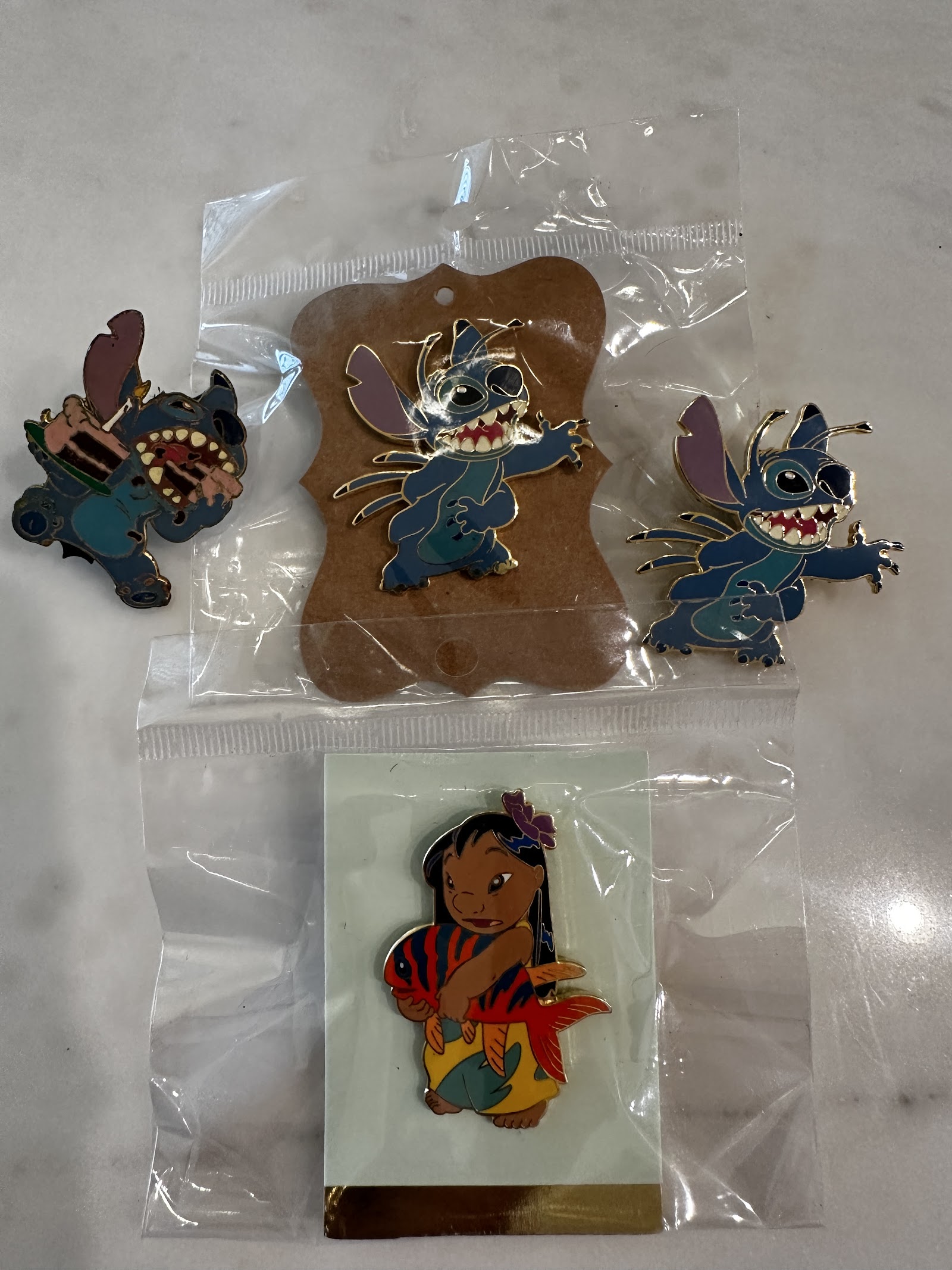 Set of four Disney Parks Lilo and Stitch enamel pins including two Stitch alien-form pins, a Lilo holding Pudge the Fish pin, and a Stitch eating pin, with two pins sealed in original polybag packaging