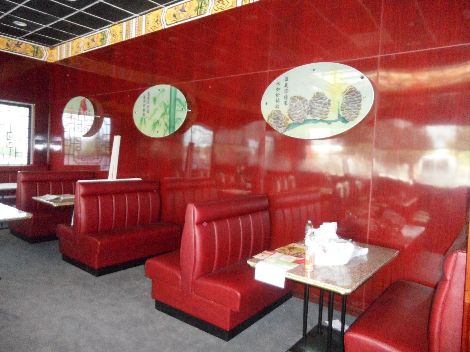 Restaurant dining area featuring red vinyl booths, glossy red wall panels, and oval nature-themed wall art.