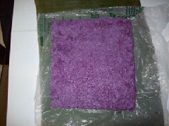 Trải 1 miếng nilon khác trên bàn, để 1/5 nếp lá cẩm trên miếng nylon ép thành 1 hình chữ nhật ngang 7.5 inches, bề dài 9 inches. Để phần nếp lá dứa có nhân lên phần nếp lá cẩm và cuộn tròn lại.