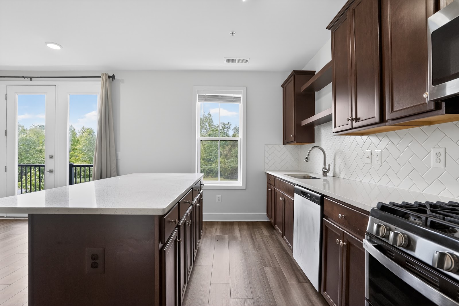 Renovated kitchen with dark walnut cabinets, quartz countertops, herringbone tile backsplash, large kitchen island, and french doors to the backyard — South Jersey home remodel