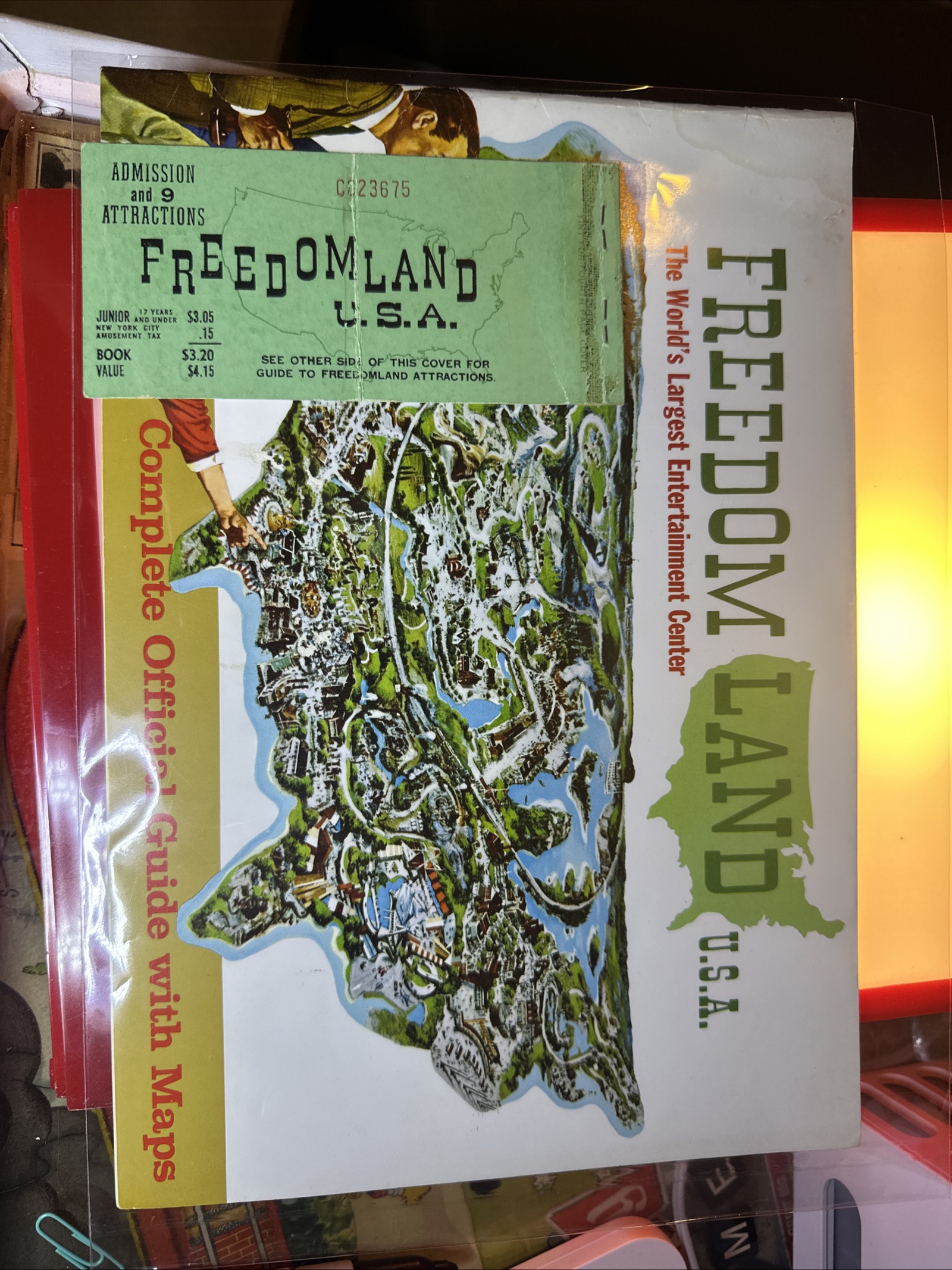 1961-1962 Freedomland U.S.A. official souvenir guide open to show bird's-eye map with vibrant green and red inks, with admission ticket book cover attached, housed in Mylar sleeve