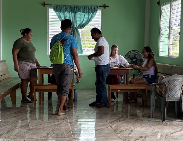 Villagers waiting and registering at intake tables inside a village church used as the clinic, Belize 2026
