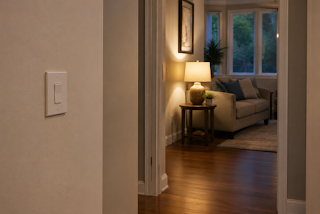 A familiar wall switch beside a clear hallway leading to a warmly lit living room, showing a simple manual way to control the light.