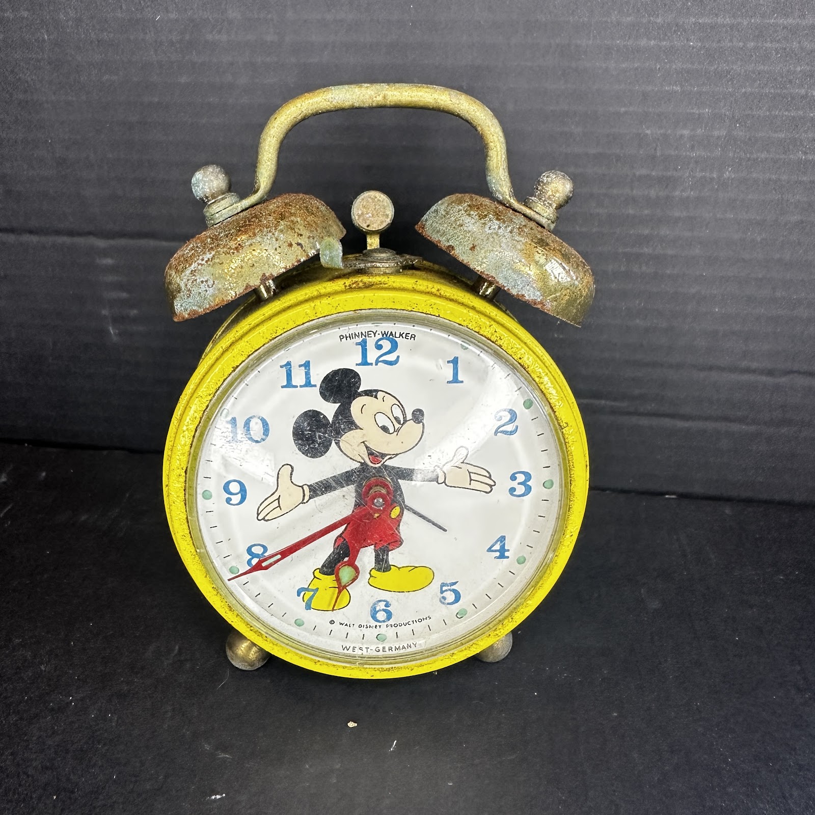 Vintage Phinney-Walker Mickey Mouse twin bell alarm clock with yellow metal casing, white dial with blue numerals, and Mickey's gloved hands as clock hands, made in West Germany circa 1950s–1960s