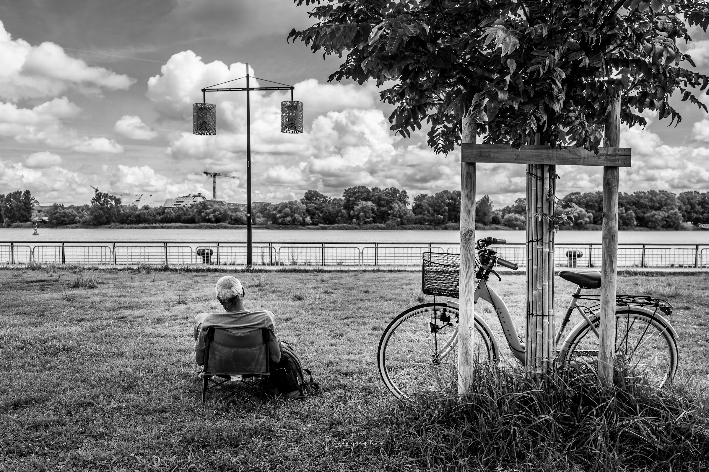 Un vélo et une personne assise face au fleuve en noir et blanc.
