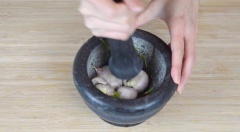 Thêm 2 trái ớt và 1 muỗng canh cuống ngò rí vào cối và giã nát chúng cho đến khi ớt chảy ra. Sau đó, thêm 4 củ hành tím vào, tiếp tục giã cho hỗn hợp nhuyễn.