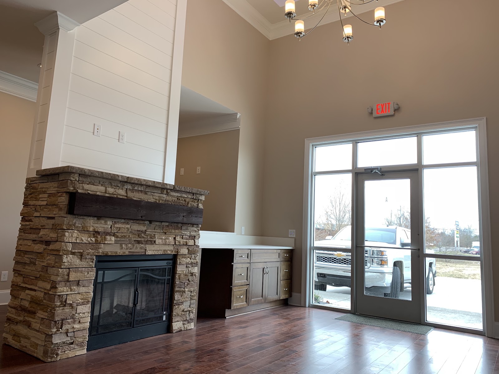 Interior view of a stone fireplace and built-in desk area. A glass door and large window show a white truck parked outside.