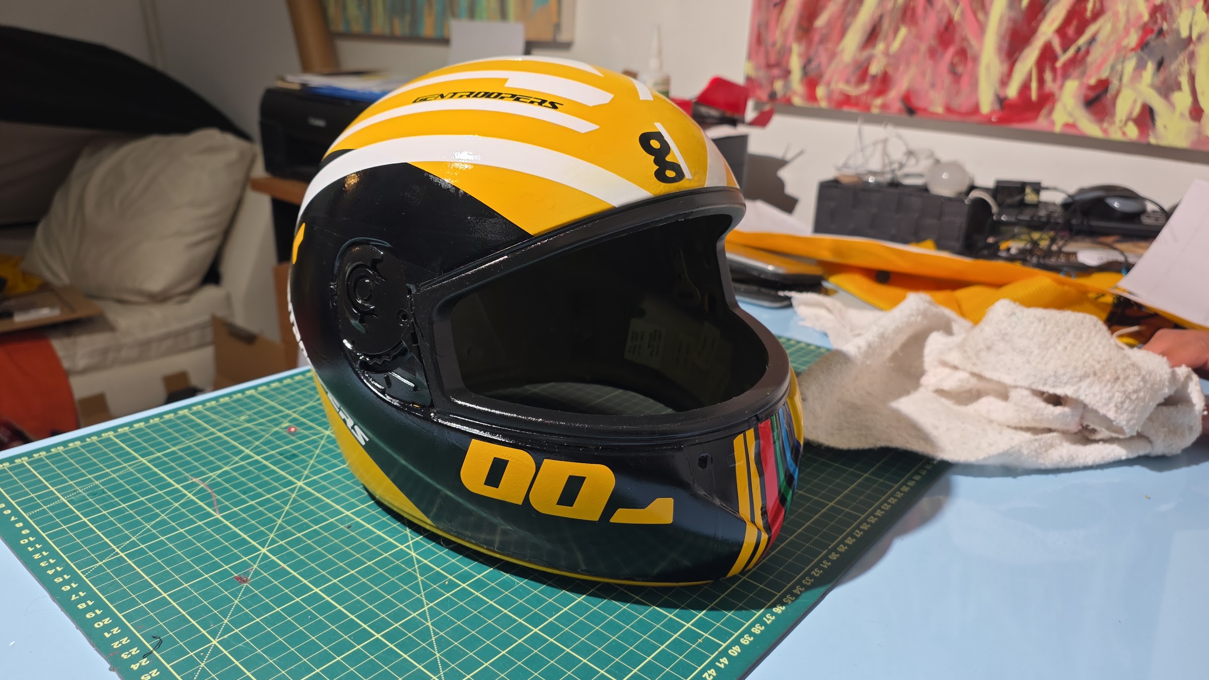 Capacete Gentroopers finalizado, vista frontal, com design amarelo, preto e branco sobre uma base de corte verde.