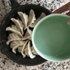 Đổ dầu ăn vào trong chảo, xếp bánh sủi cảo cào chảo, rót nửa chén nước lọc vào. Đun lửa to khoảng 5 phút rồi hạ nhỏ lửa cho bánh chín thơm như ý là được (đáy bánh có màu vàng và giòn). Rắc thêm ít mè đen, hành lá và ớt.