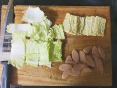 Thái các nguyên liệu còn lại, gồm cải thảo, chả cá Hàn quốc, xúc xích thành miếng nhỏ vừa ăn. xếp mì gói vào trong hộp, tiếp đến là chả cá, xúc xích và cải thảo, và trứng đã luộc chín.