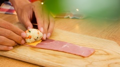 Vo cơm thành những viên tròn nặng khoảng 35gr. Phô mai cheddar lát đem cắt làm 4. Trải 1 lát ba rọi nạc xông khói ra thớt, xếp 1 miếng phô mai cheddar lên trên, đặt viên cơm rồi gói cơm lại theo hình tam giác sau cho miếng ba rọi bao bọc hết phần cơm. Nếu thiếu có thể bổ sung thêm ba rọi để gói cơm kỹ hơn.