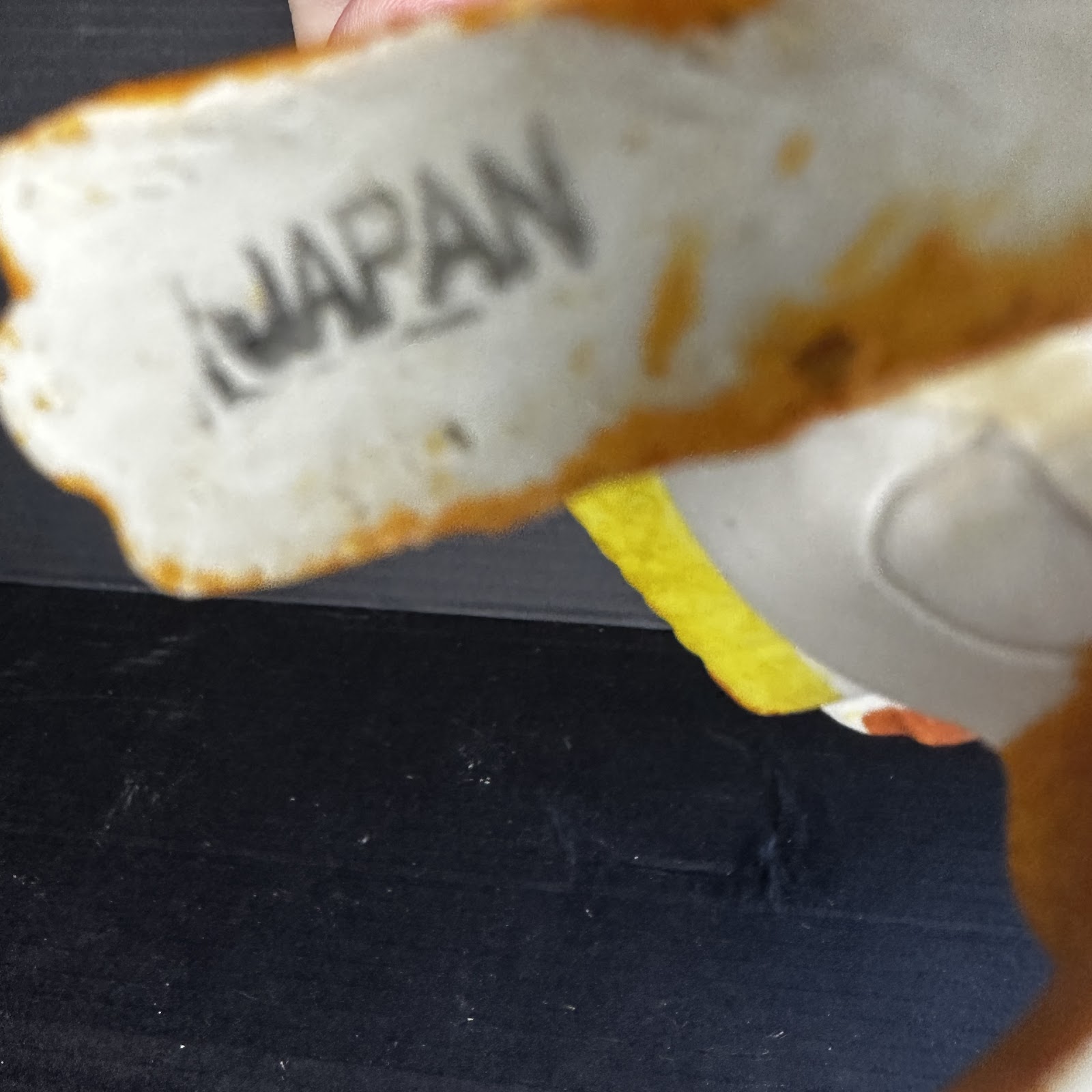 Fragment of a 1970s Japanese bisque ceramic Disney figurine showing yellow, brown, and white paint with visible chipping and a "Made in Japan" stamp on the unglazed base