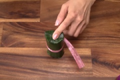 Gấp lá chuối ở 1 đầu bánh tét, dựng đứng đòn bánh tét chuối. Vỗ nhẹ, dùng muỗng nén nhẹ nếp ở đầu cho bằng phẳng. Cắt bỏ bớt phần lá chuối thừa. Dùng 2 ngón tay ấn 1 bên lá xuống mặt phẳng nếp trước đó, gấp tiếp theo thứ tự phần lá bên trái, đến bên phải, cuối cùng là phần lá đối diện. Tương tự cho đầu bánh tét chuối còn lại. Sau đó buộc dây chữ thập cố định 2 đầu. Tháo bỏ dây màu đỏ lúc đầu. Tiến hành buộc dây theo từng vỏng nhé. Phần dây buộc thừa gom về một chỗ như hình. Tương tự cho đến hết lá và nếp bánh nhé.