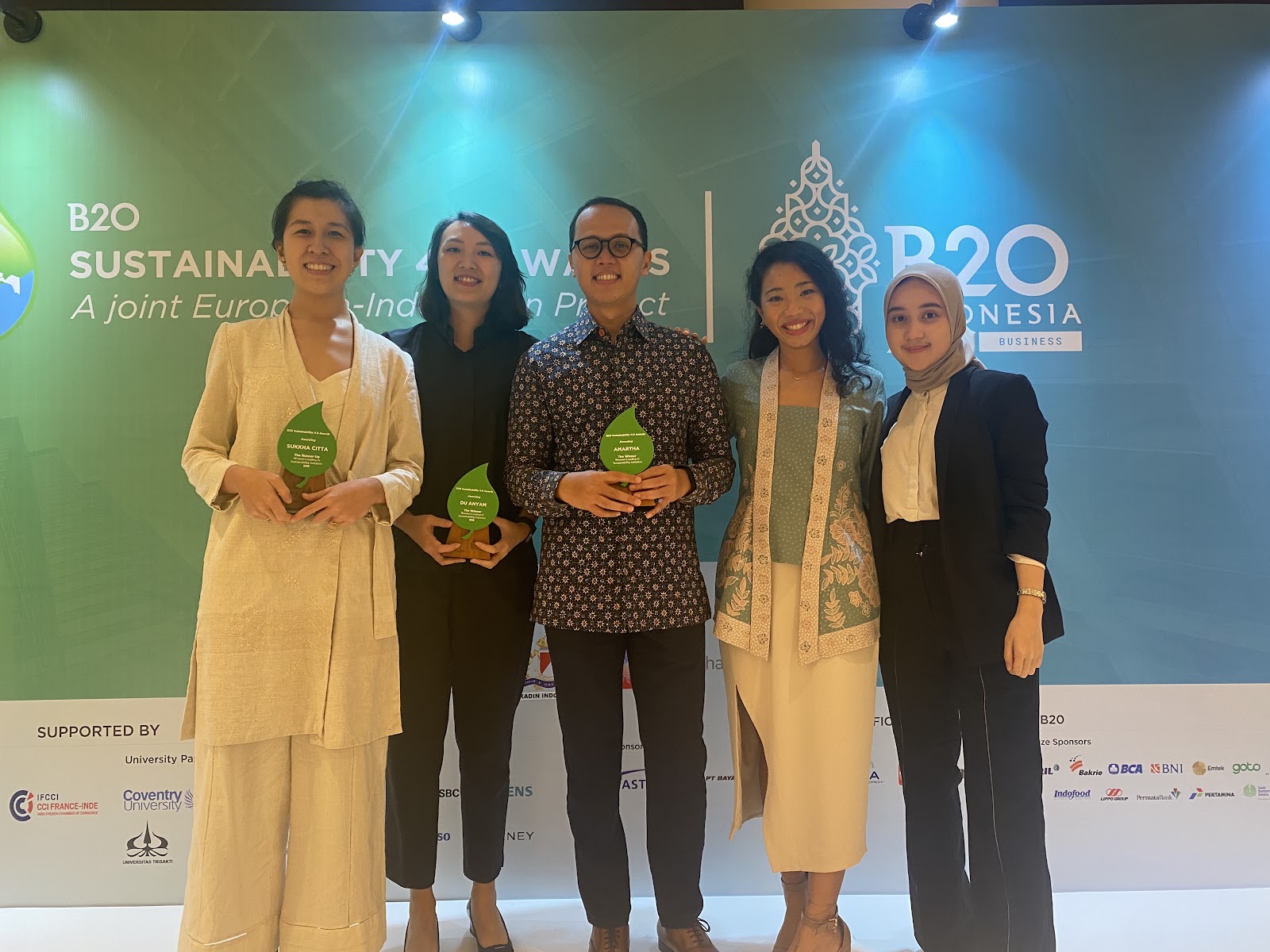 Representatives from Sukkhacitta, Duanyam, Amartha, CarbonEthics, and Hearme posing in front of green banner of B20 Indonesia Sustainability Awards