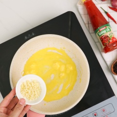 Bắt chảo lên bếp, cho 20gr bơ vào nấu tan, cho tiếp 1 muỗng canh tỏi băm và 50gr hành tây thái múi cau vào phi thơm, sau đó trút phần bạch tuộc đã ướp vào xào săn với lửa lớn.