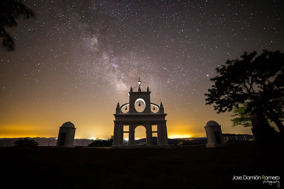 White viewing arch at Peña de Arias Montano beneath the Milky Way and a sky filled with stars.