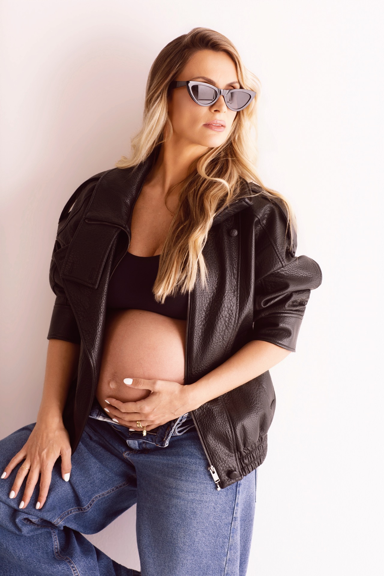 Camila Eccel em ensaio de gestante com jeans, jaqueta preta e �culos.