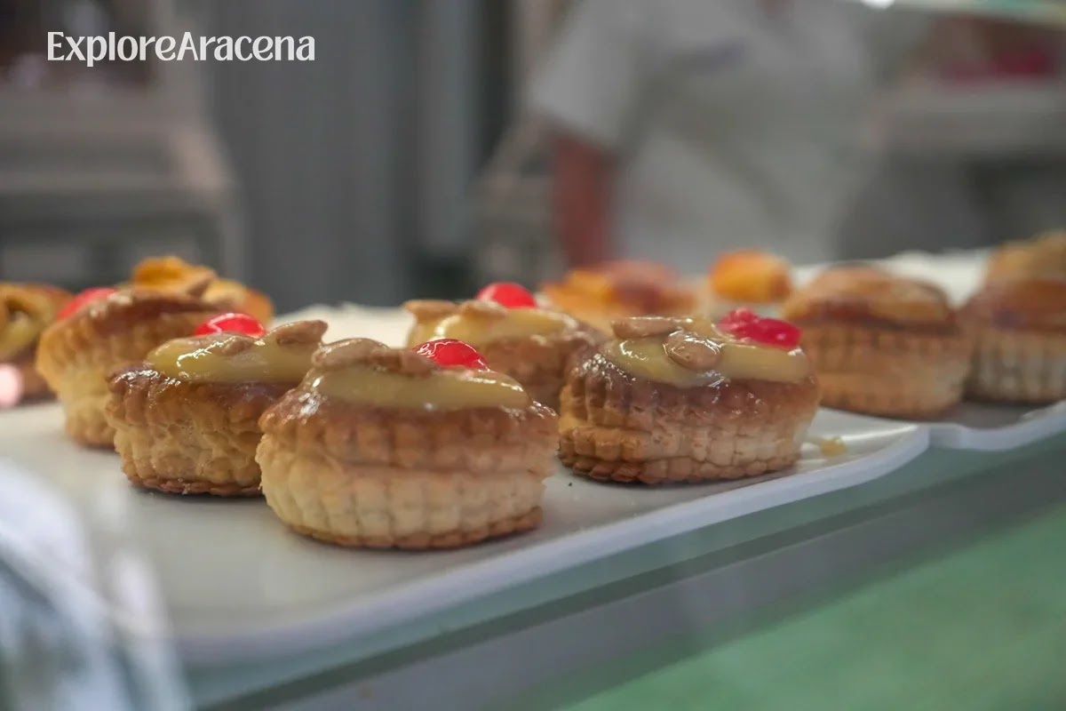 Custard-filled puff pastry tarts arranged inside a bakery display in Aracena.