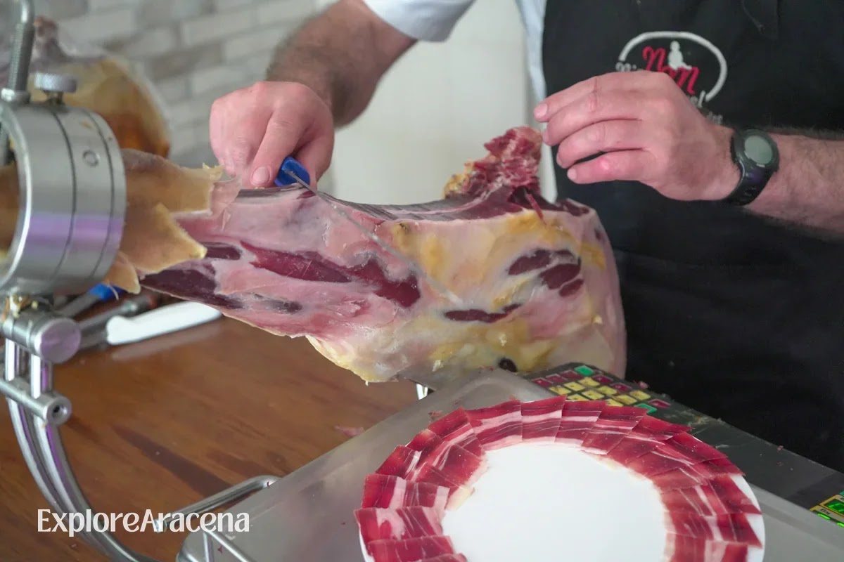 A cortador slicing jamón by hand onto a plate arranged with two circles of thin slices.