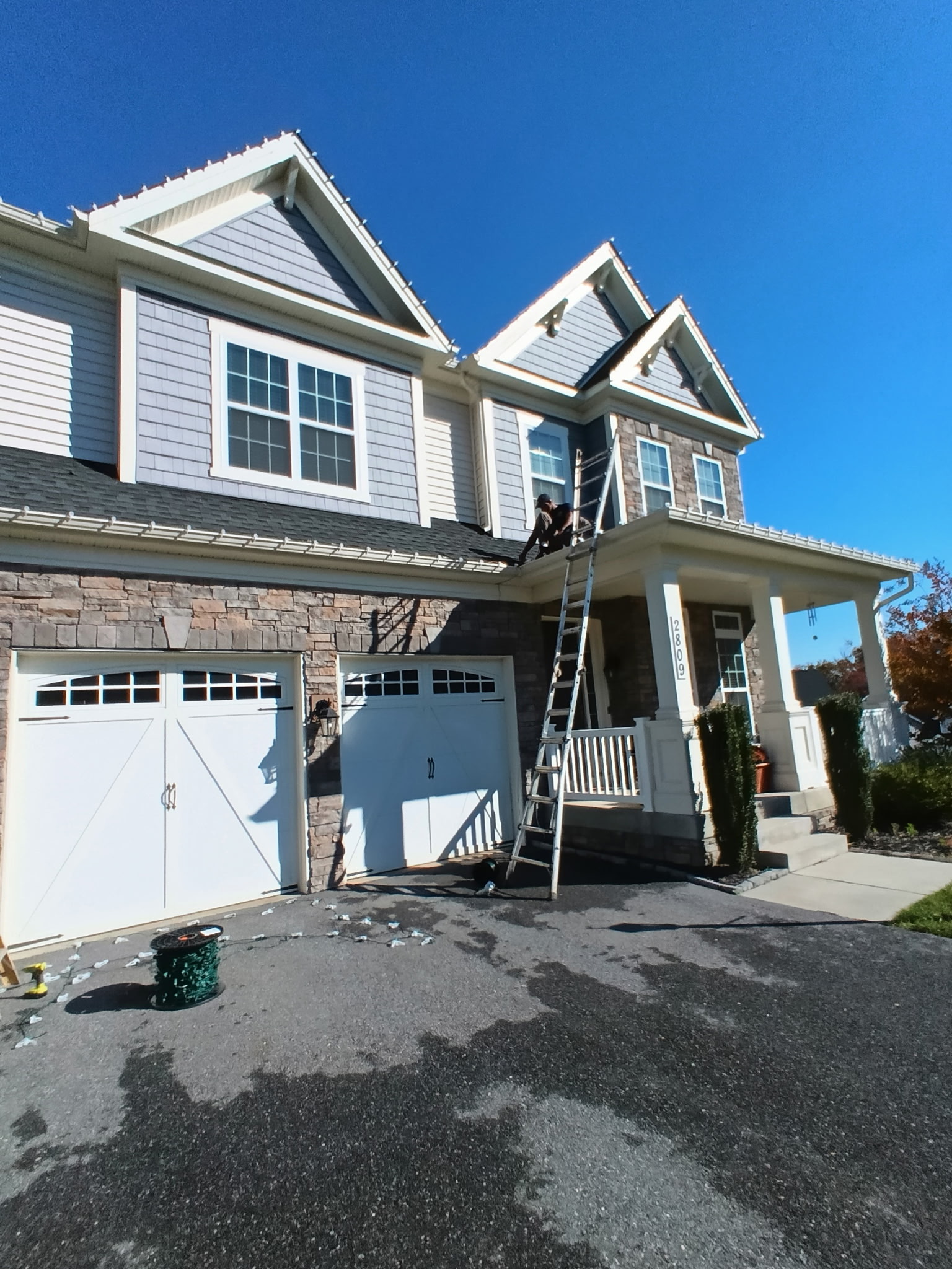 Holiday lighting installer working from a ladder on a two-story Maryland home