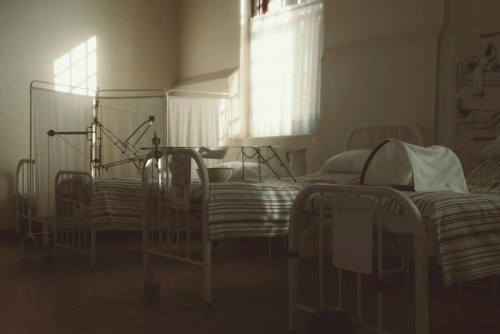 Dimly lit vintage hospital room featuring empty beds and medical equipment, creating a nostalgic atmosphere.